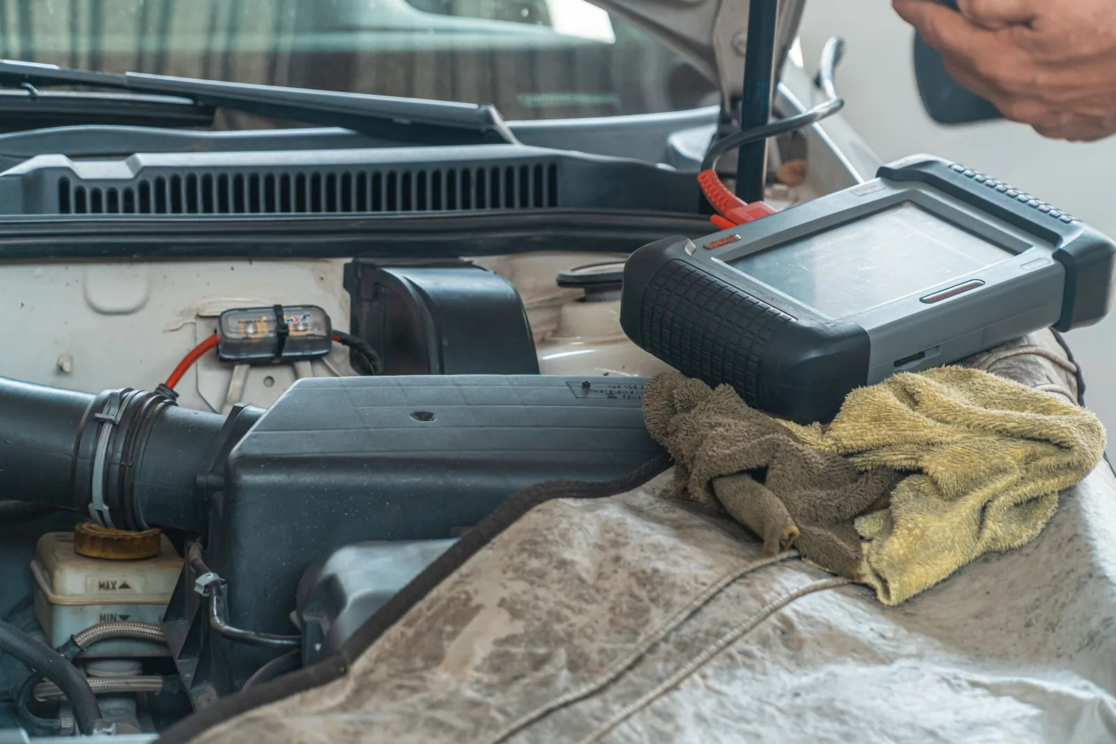 A handheld diagnostic tablet resting on an open engine bay during a fault scan