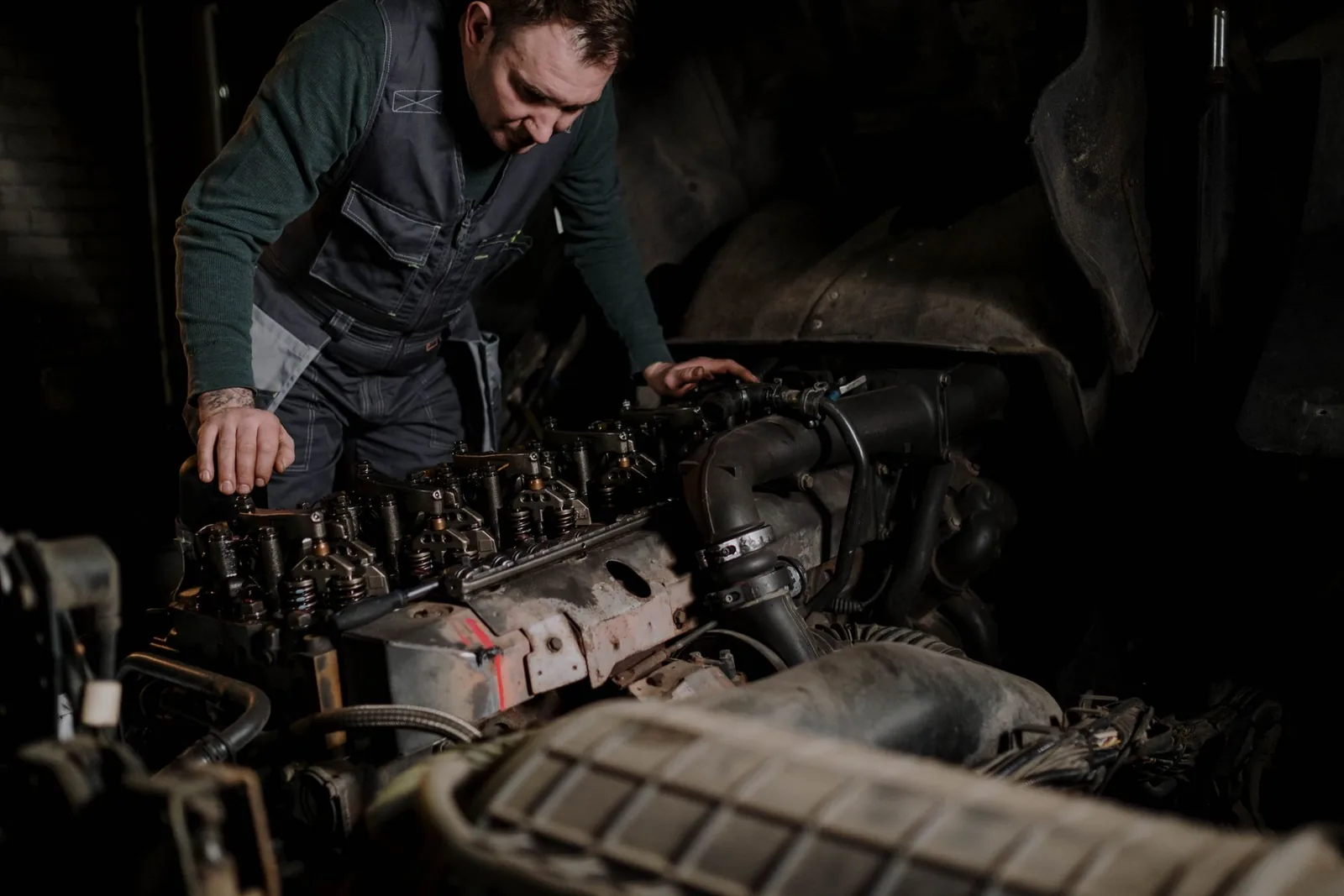 A technician working over an open diesel engine in a dimly lit workshop