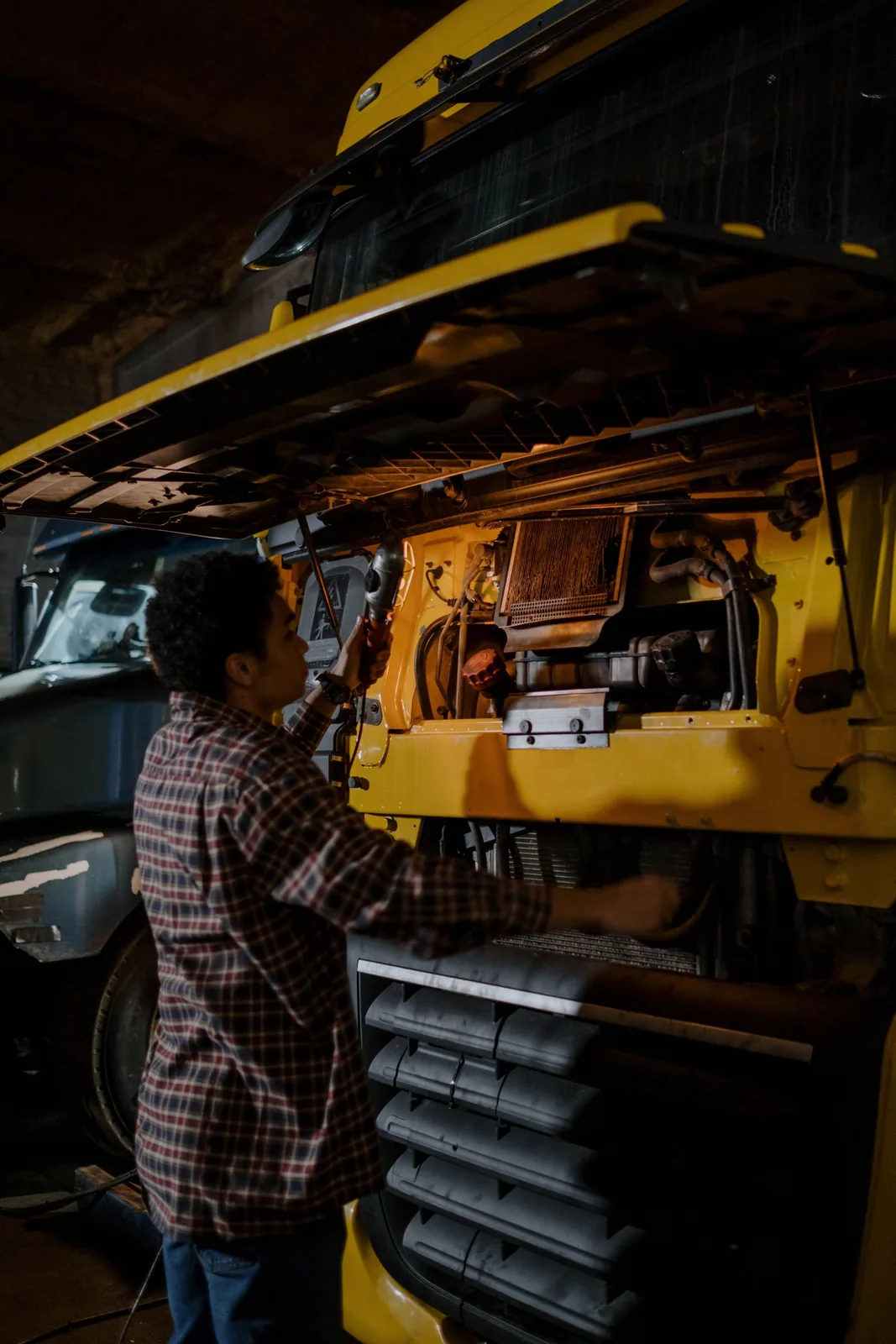 A technician reaching into the engine compartment of a heavy commercial truck