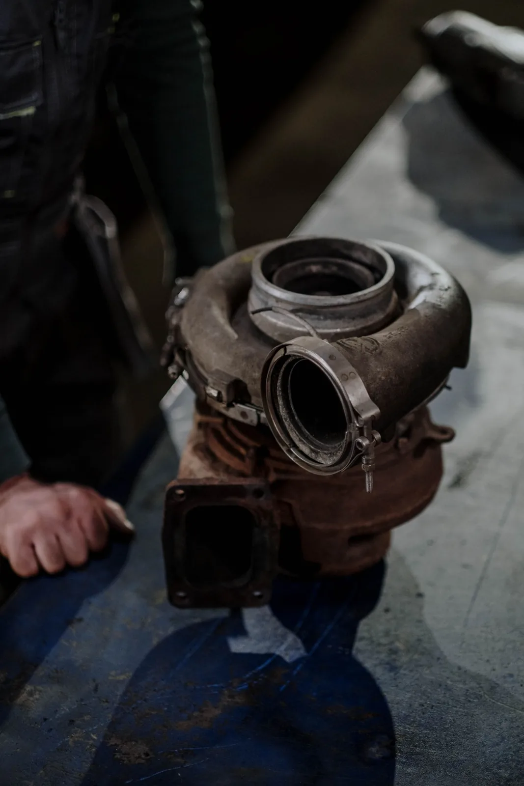A removed turbocharger held in both hands, its housing carbon-stained from exhaust gas